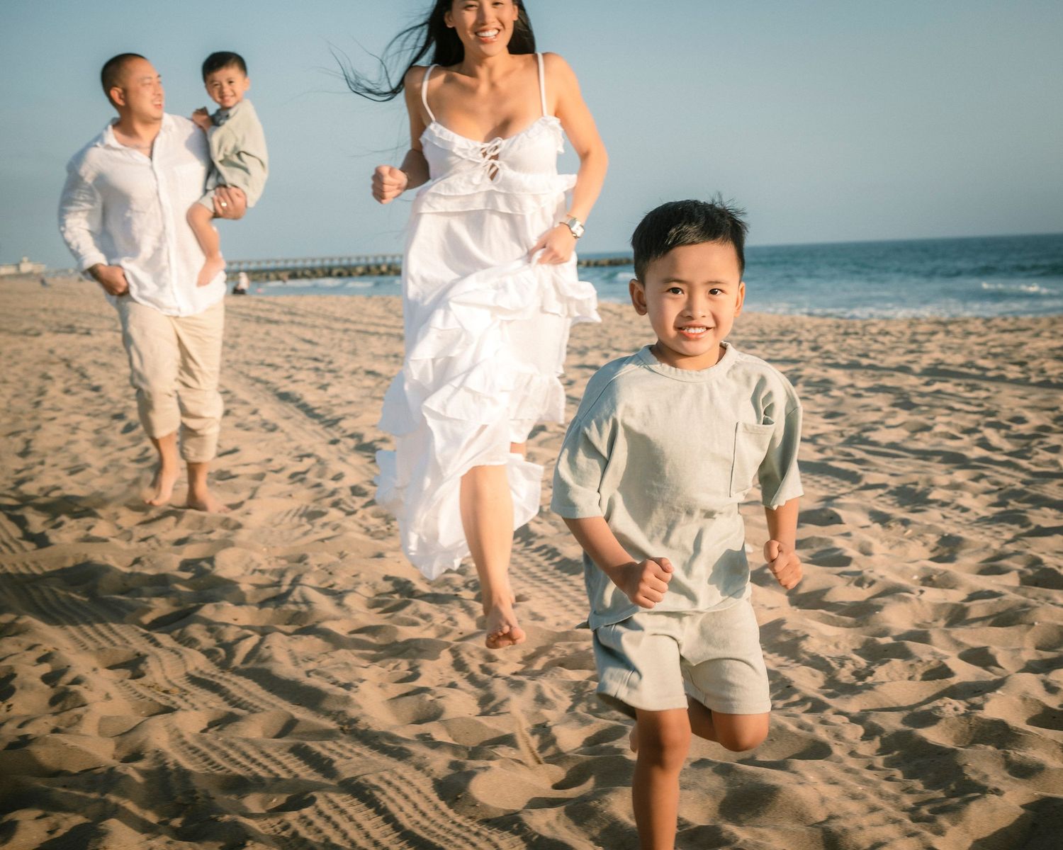 A joyful Asian family running on a sunny beach, with a young boy smiling in the foreground.