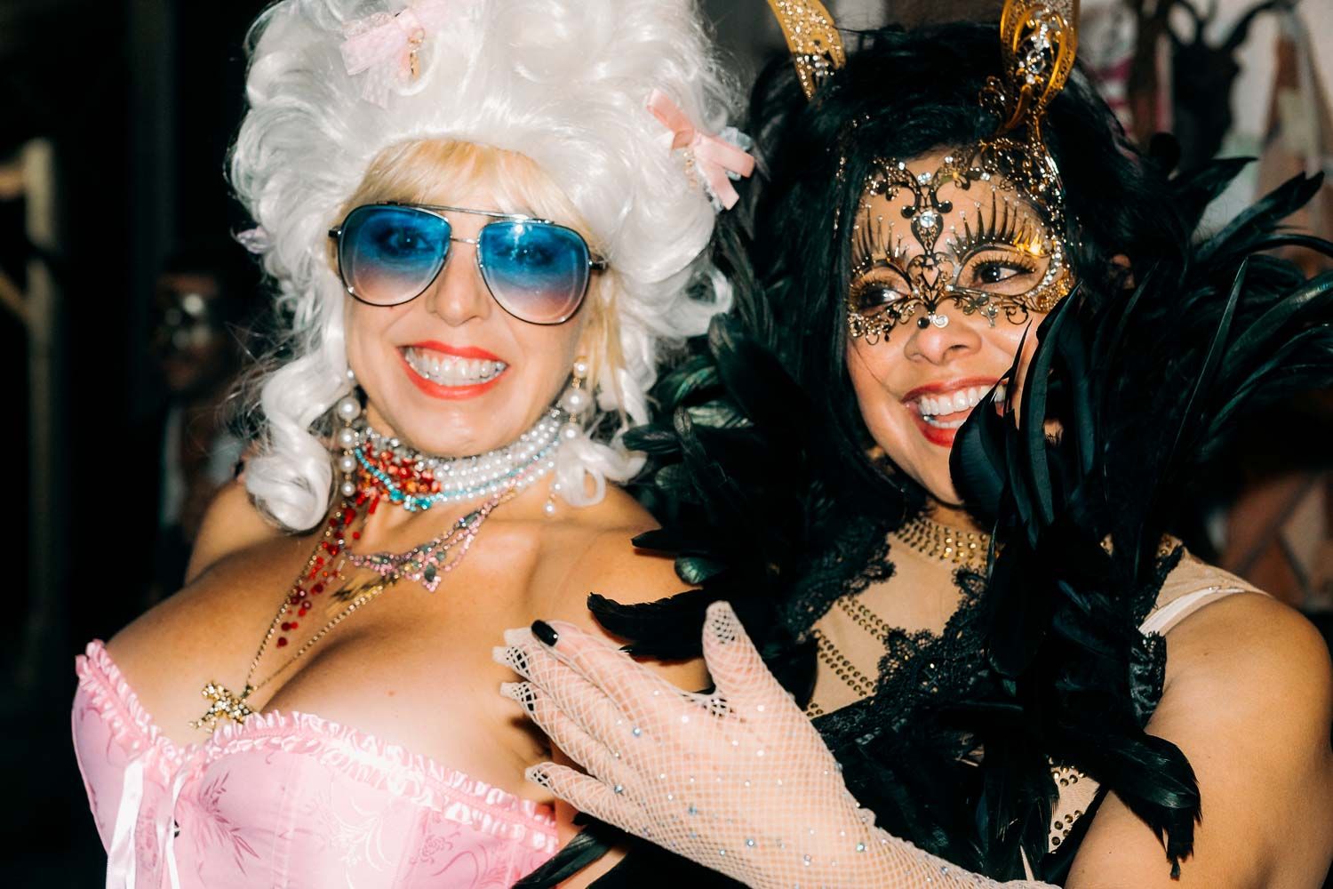 Two women in elaborate masquerade costumes posing together at a festive costume party.