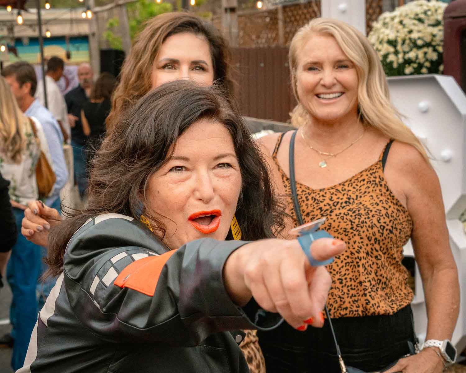 Woman in leather jacket pointing and smiling at an outdoor social gathering event.