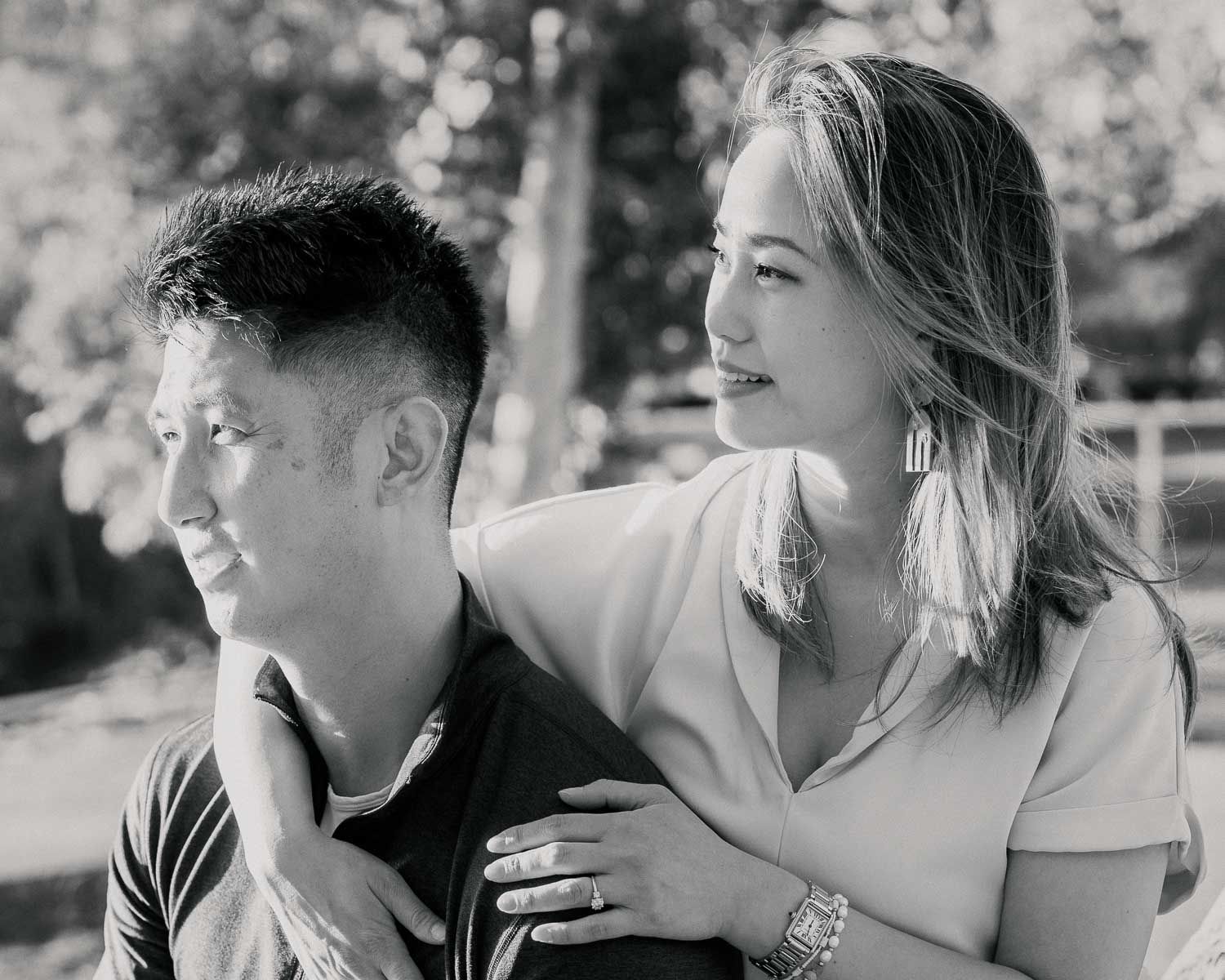 Black and white portrait of a couple sitting together outdoors among trees.