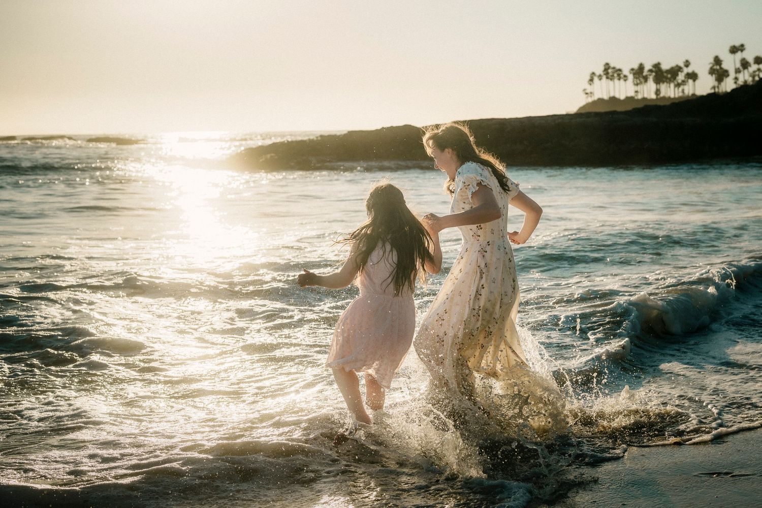 Mother and daughter splashing joyfully in ocean waves at sunset.