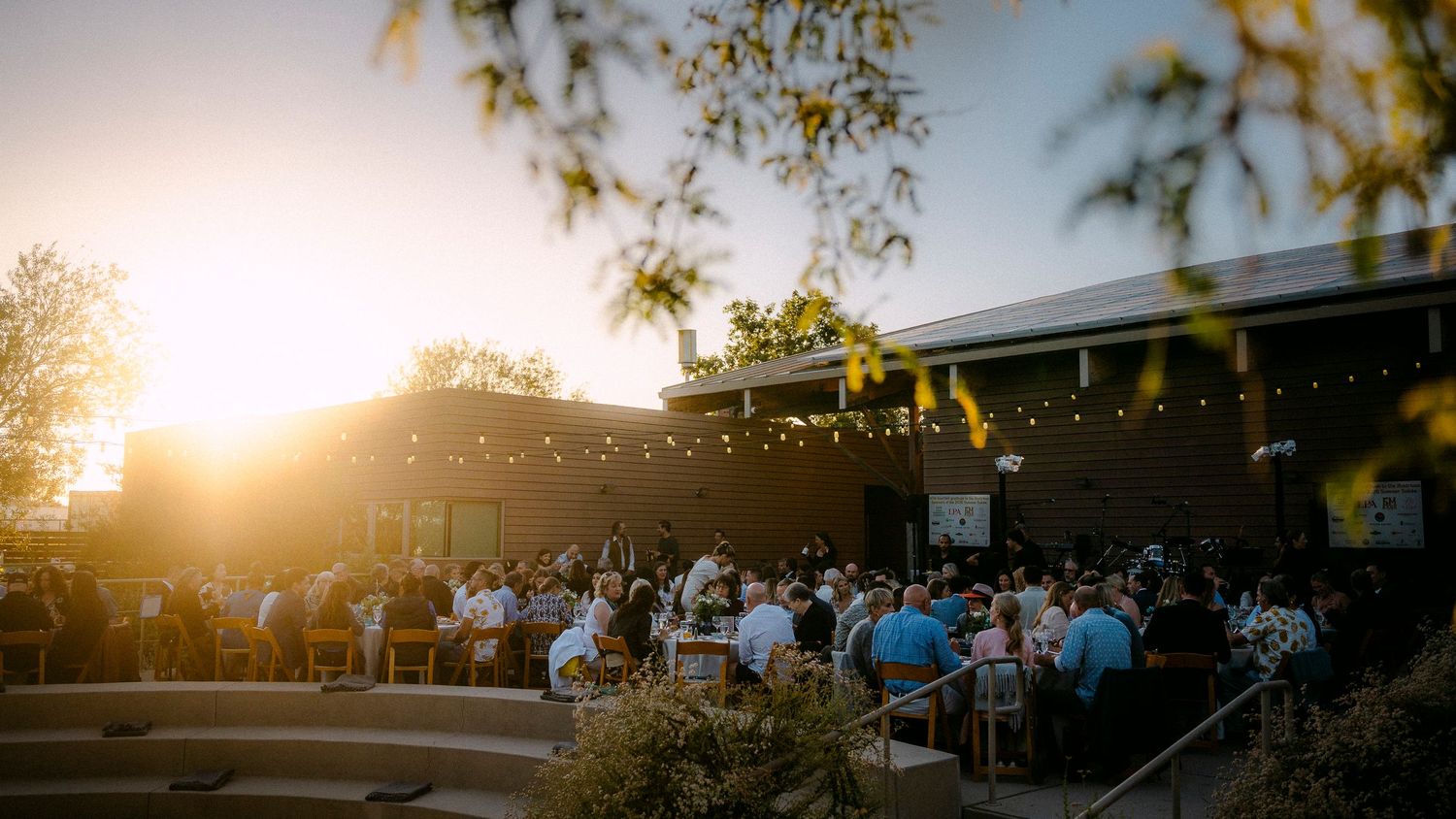 Guests gather at an outdoor evening event venue with string lights at golden hour sunset.