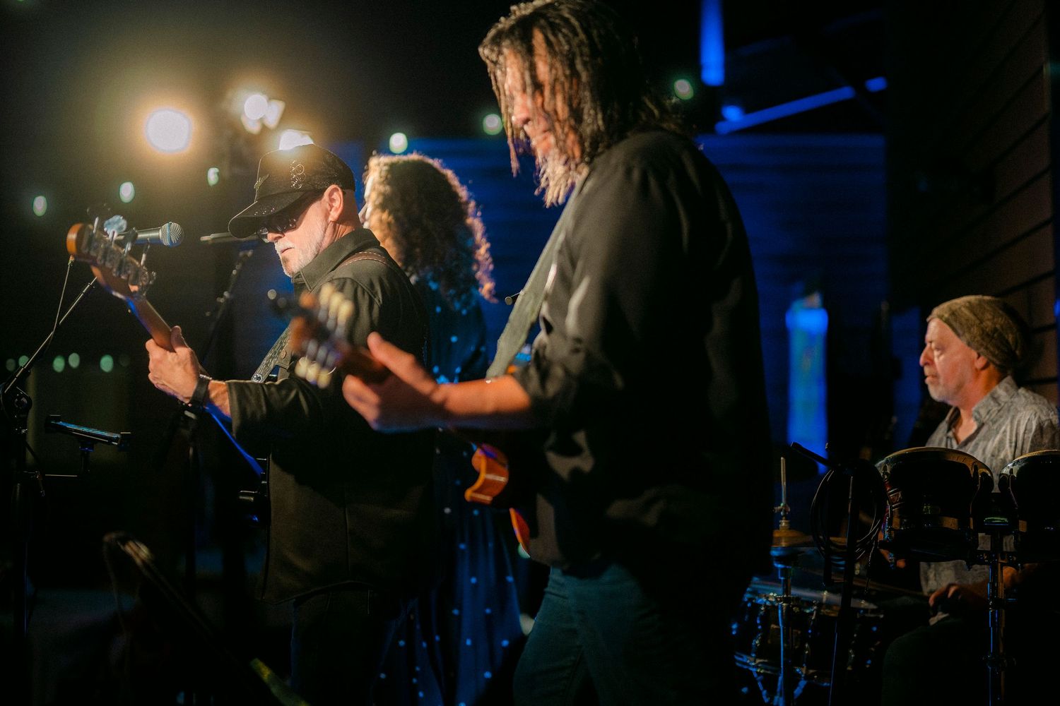 Live band performing on a dimly lit stage with electric guitars and drums at a night event.