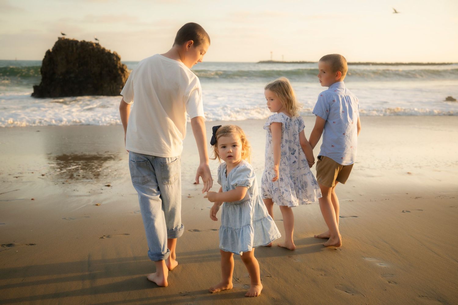 Father and three children playing on a sandy beach at golden sunset near ocean waves.