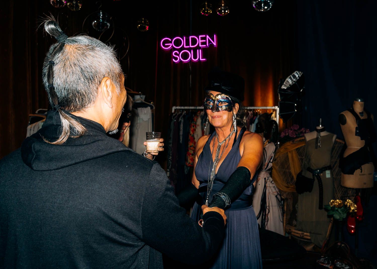 Woman wearing a masquerade mask at a Golden Soul neon-lit event party.