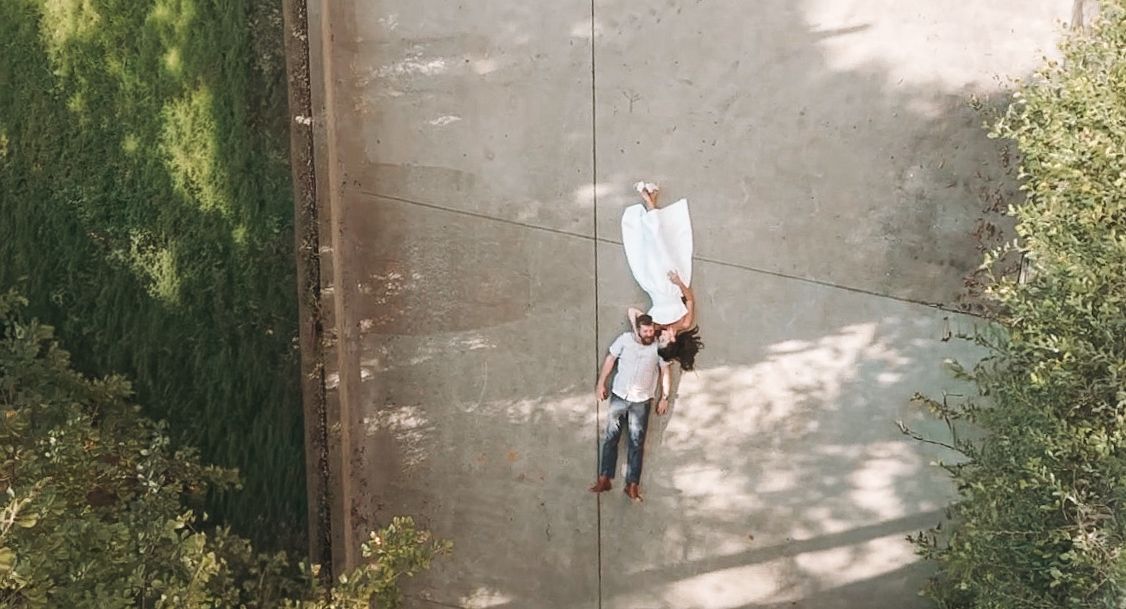 Aerial view of a couple lying on a concrete path surrounded by lush green hedges and trees.
