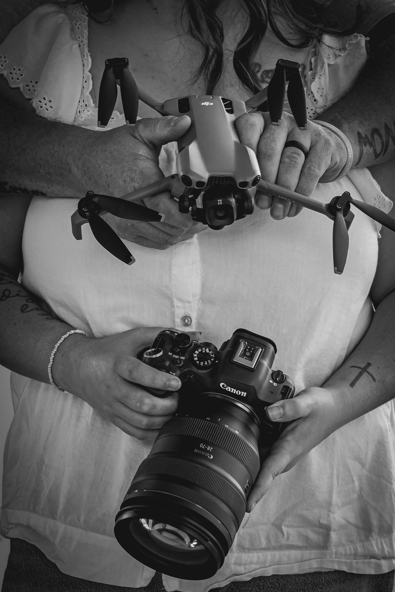 A couple holds a Canon DSLR camera and drone together in a black and white close-up shot.