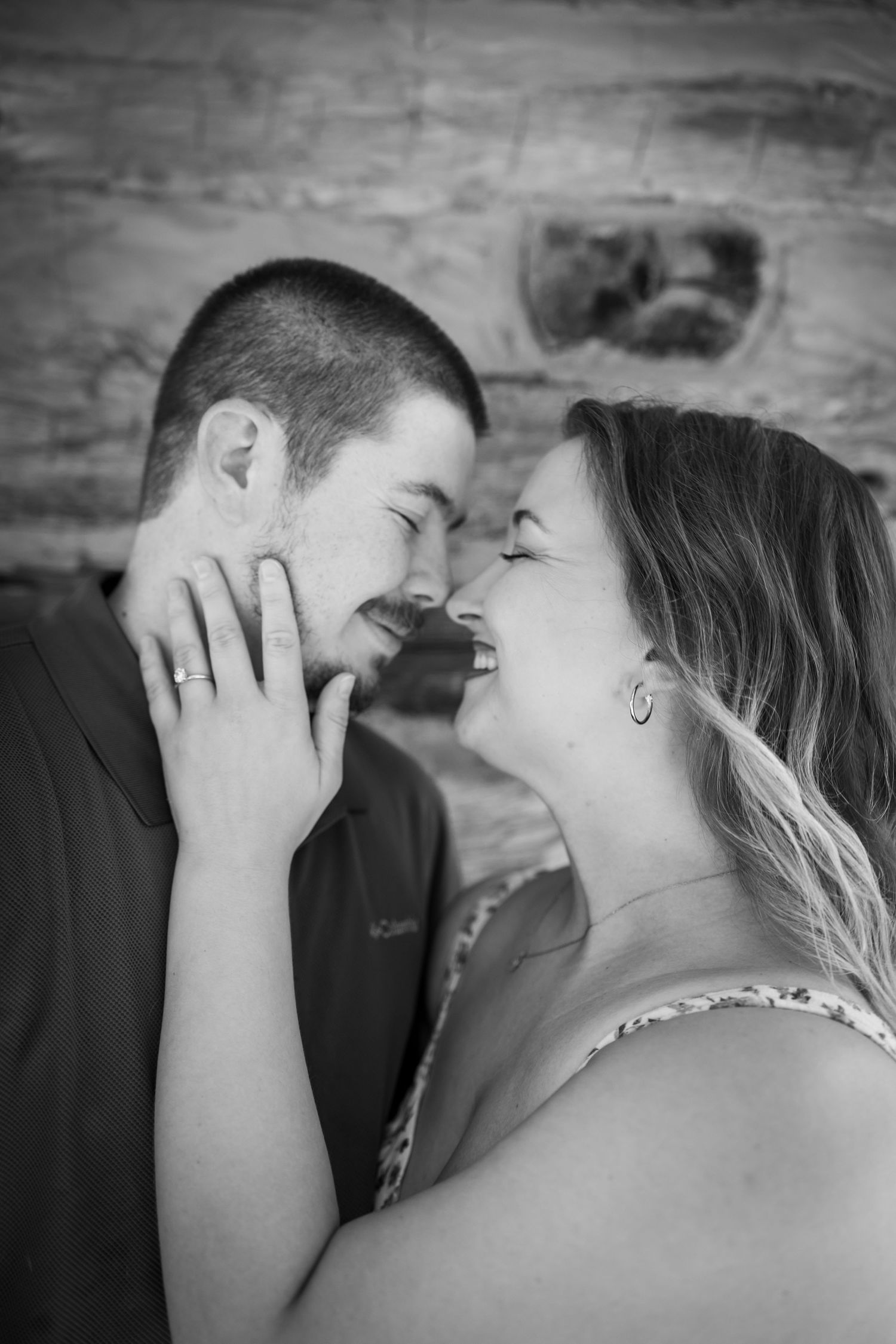 Black and white photo of laughing engaged couple embracing with engagement ring visible.