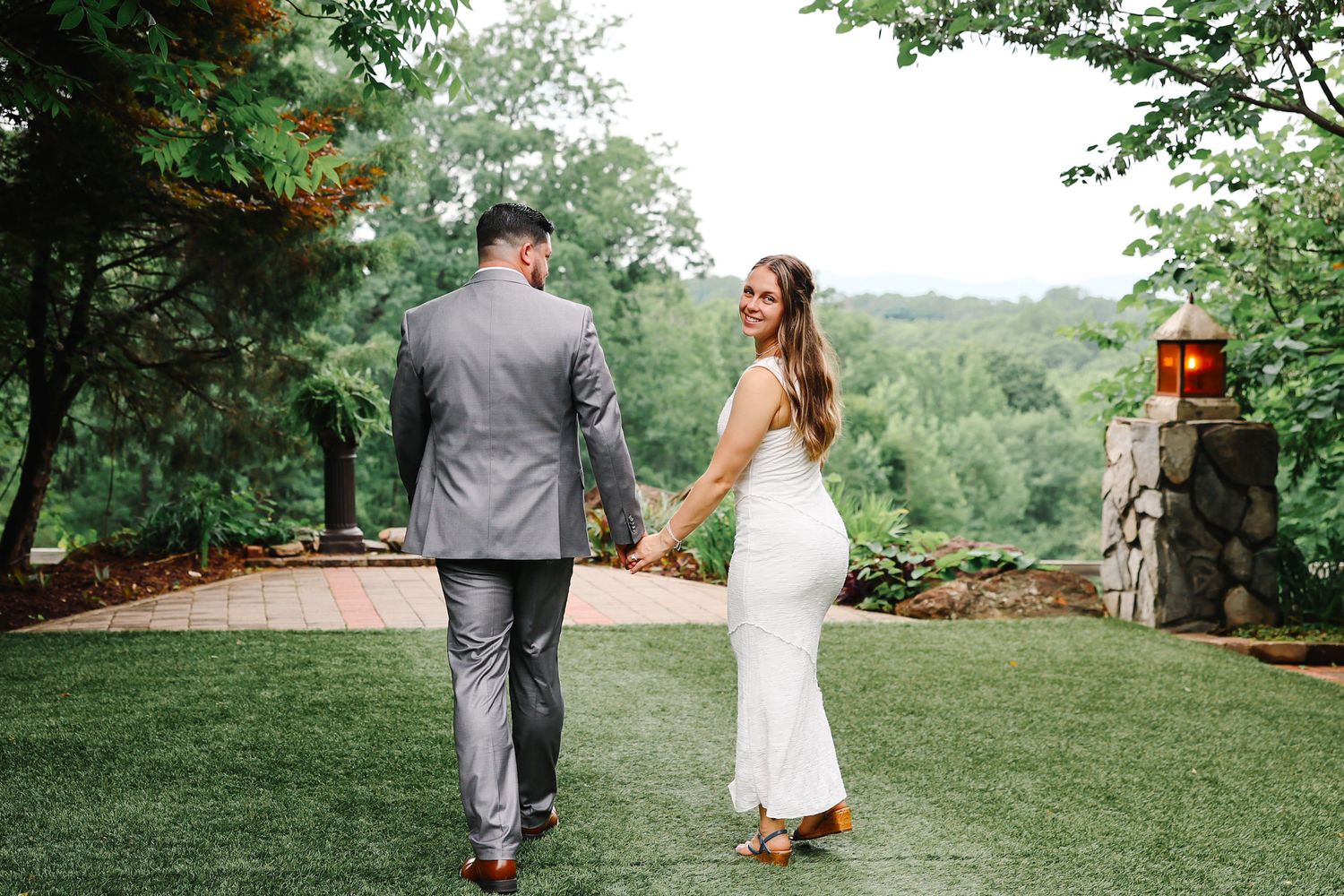 Bride and groom walking hand in hand through lush green garden on their wedding day.