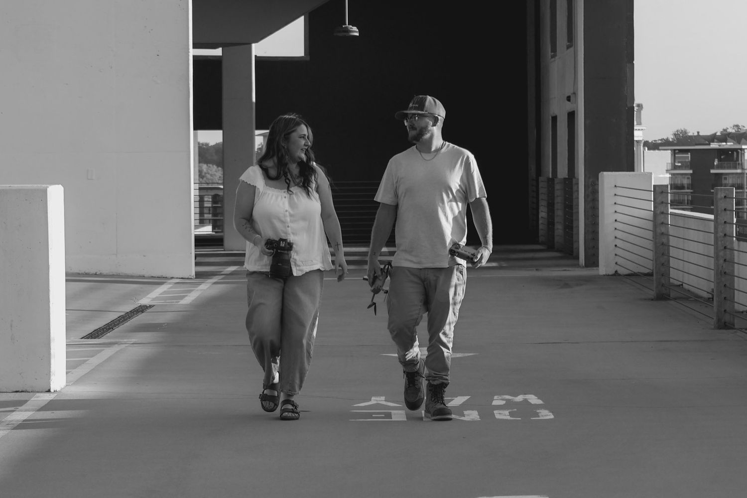 Black and white photo of a couple walking together on a sidewalk near a building.