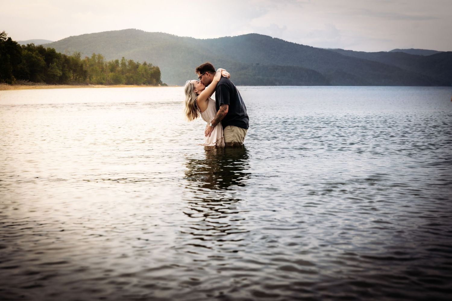 Romantic couple kissing while standing in a serene mountain lake.