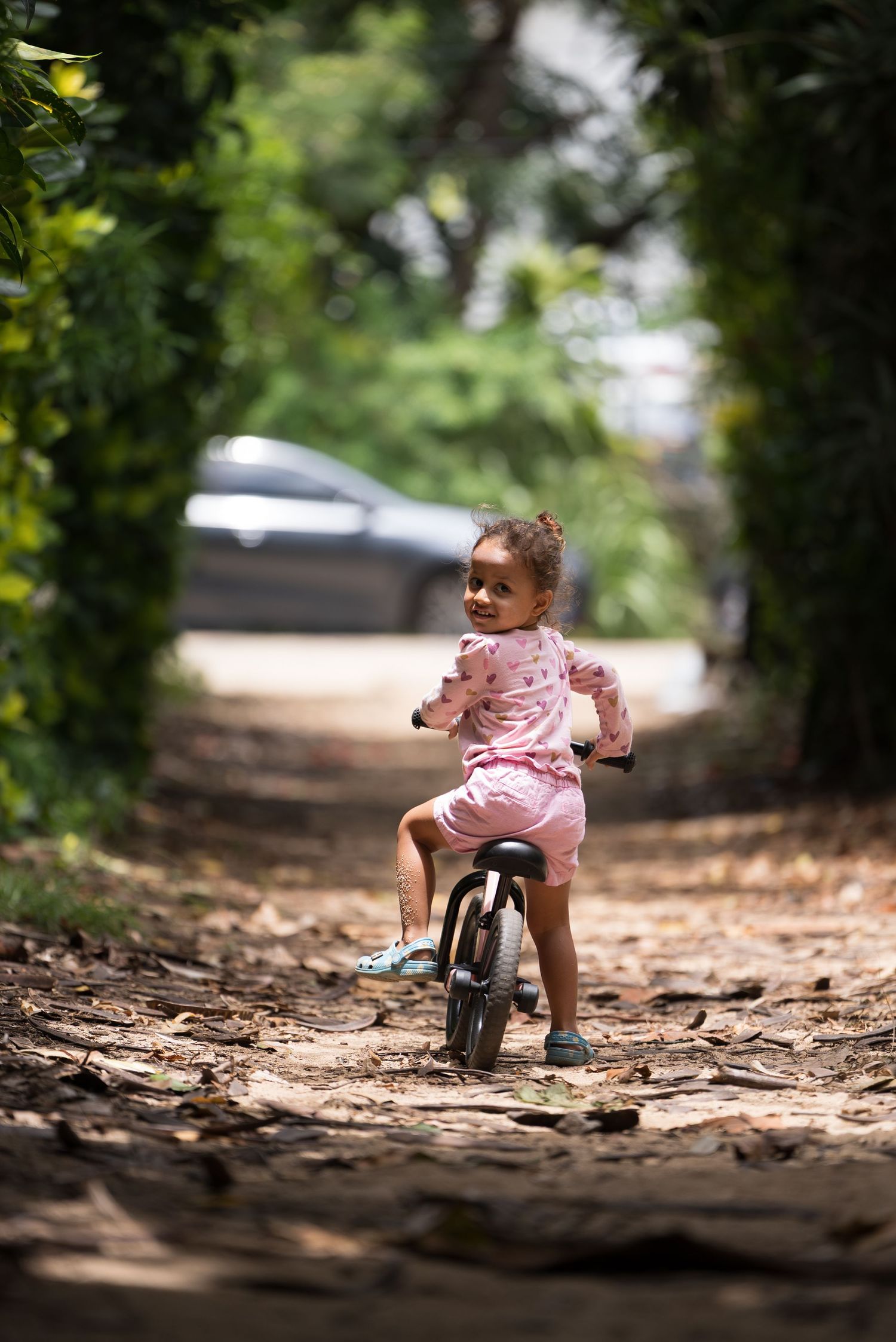 Young child looking back while riding a balance bike along a shaded path