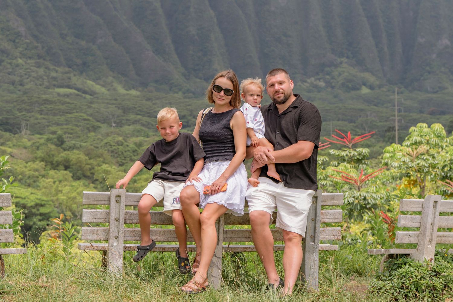 Family of four seated together outdoors with green mountain cliffs behind them