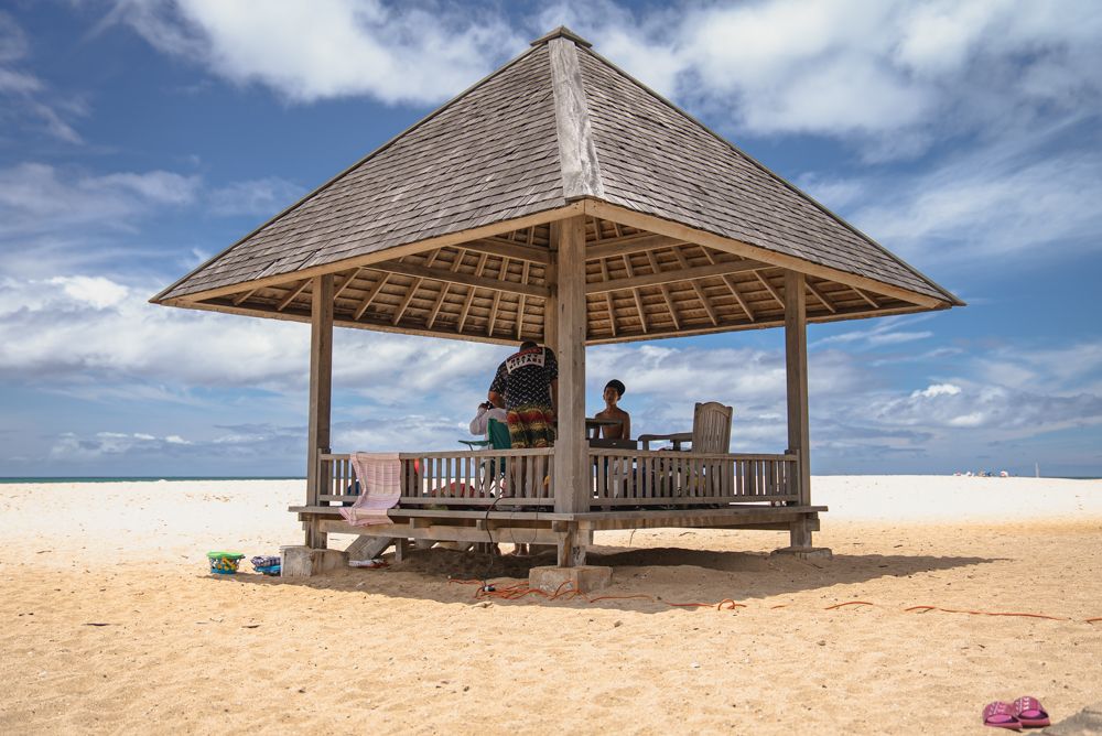 Beach pavilion on Oʻahu with a person seated beneath it under a blue sky.