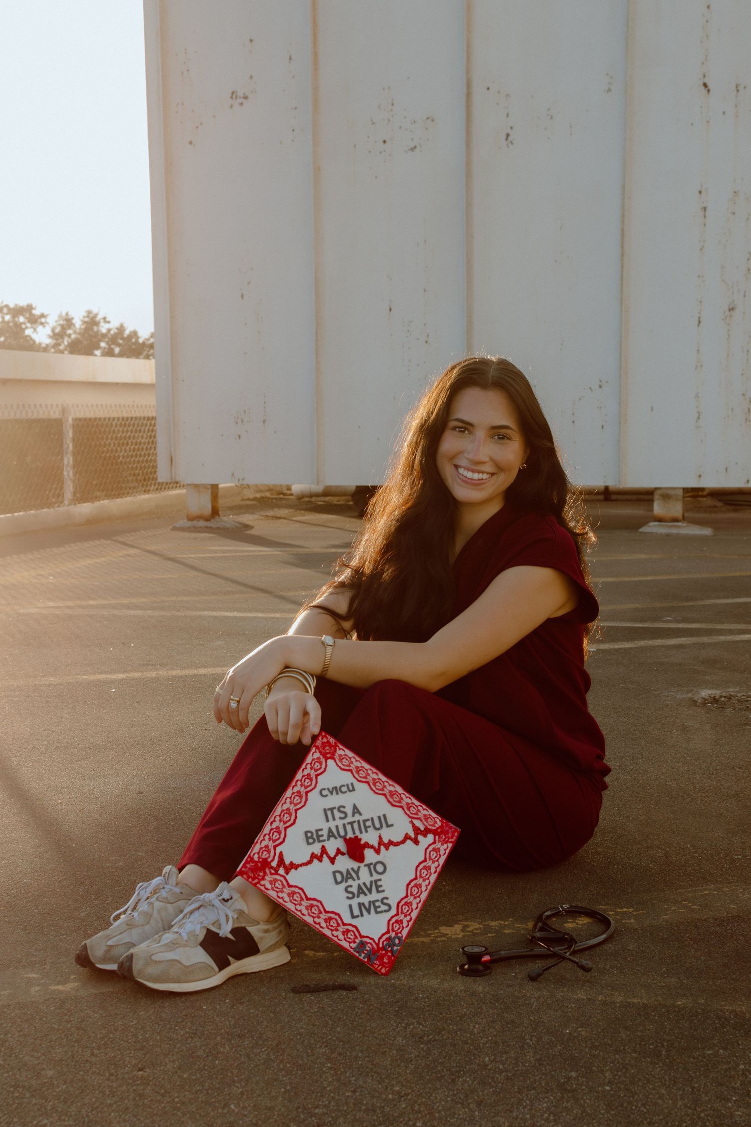 Smiling nursing graduate in red scrubs sitting with a decorated graduation cap reading It's a Beautiful Day to Save Lives.