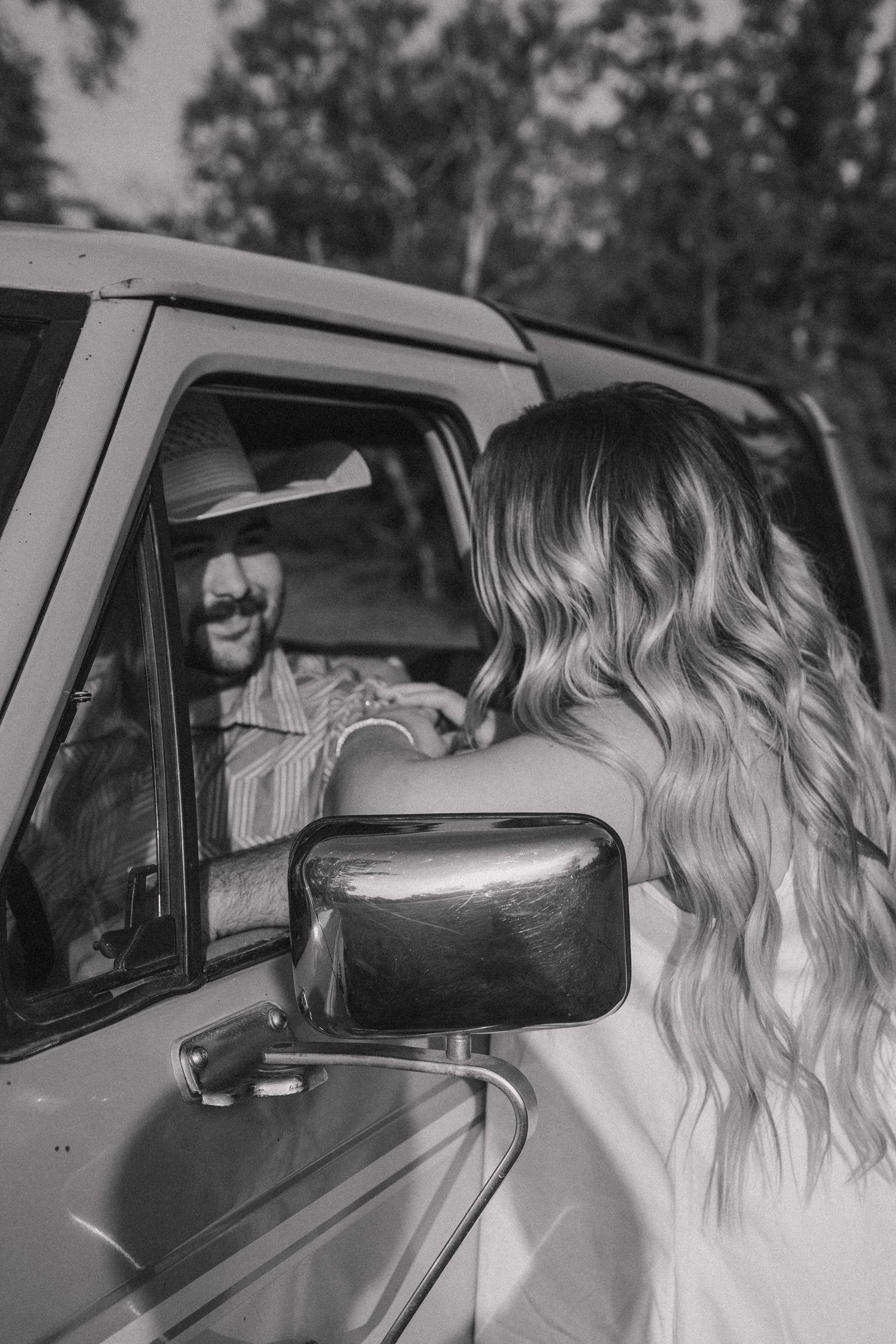 Black and white photo of a smiling man in a cowboy hat leaning out of a truck window.