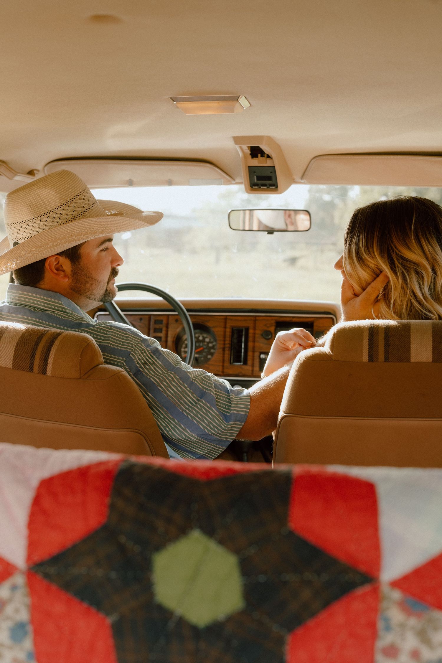 A man in a cowboy hat and woman share an intimate moment while sitting in the front seat of a vintage vehicle.