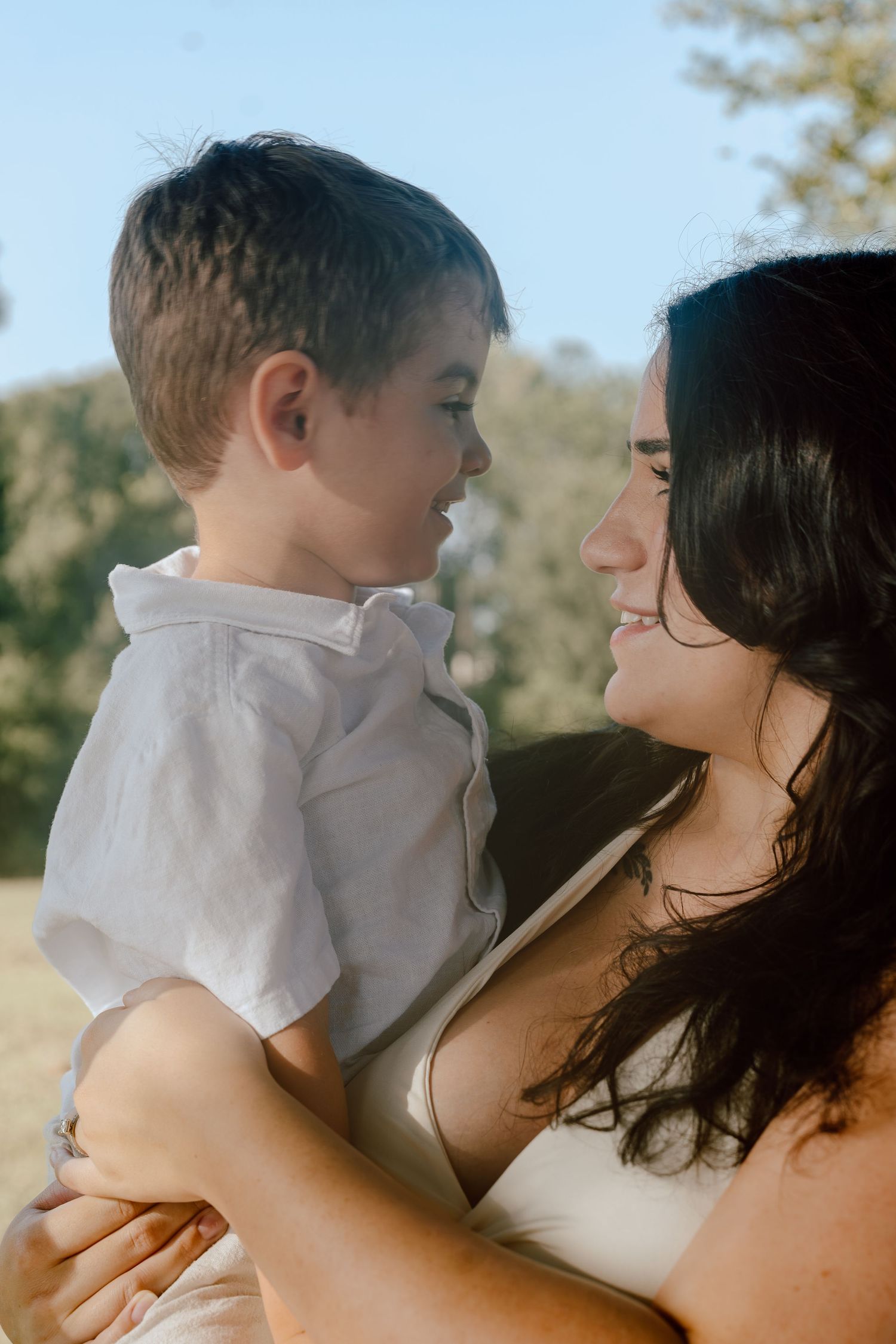 Mother and young son smiling at each other in a tender outdoor portrait in natural sunlight.