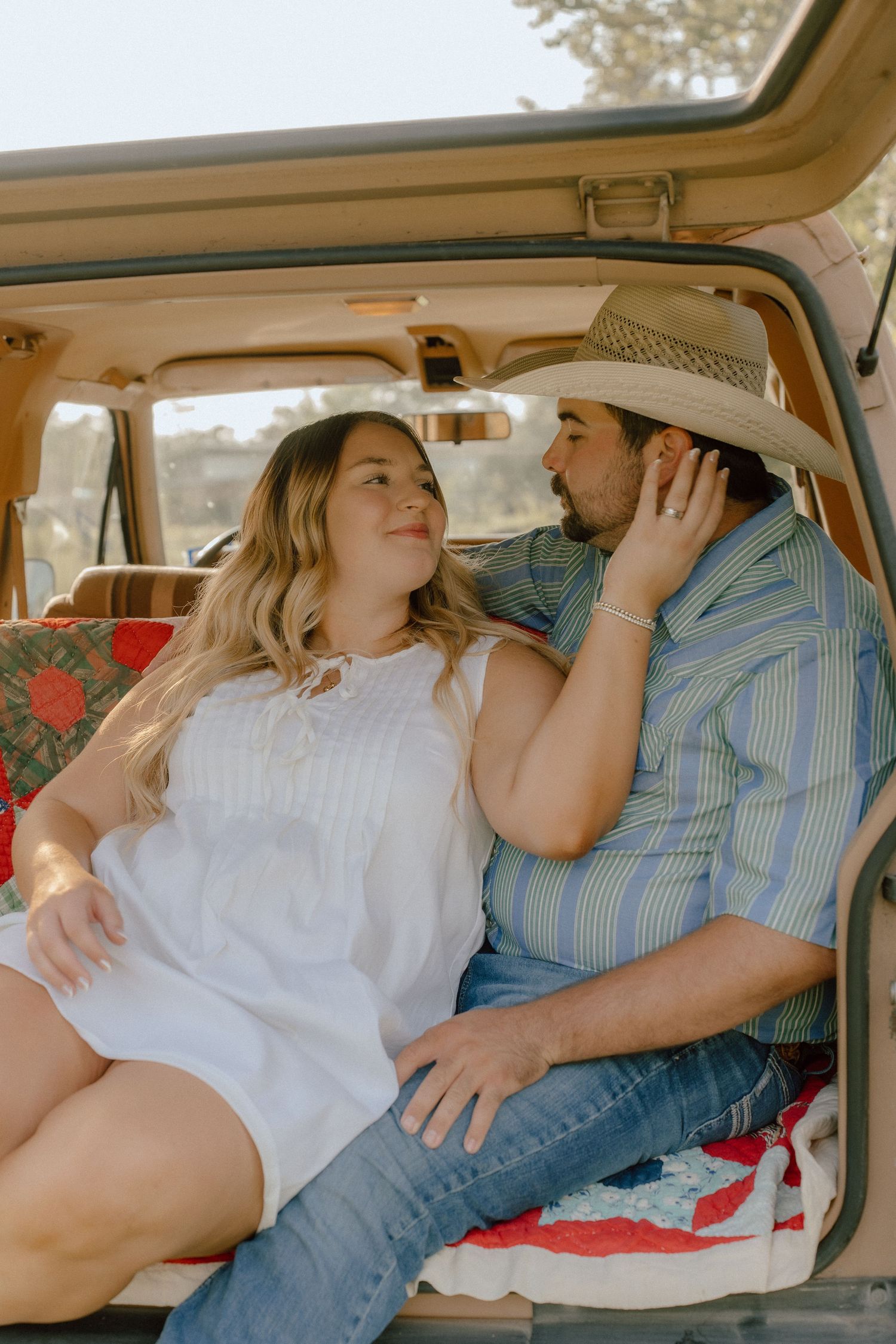 Couple sharing a tender moment sitting in the back of a vintage SUV together.