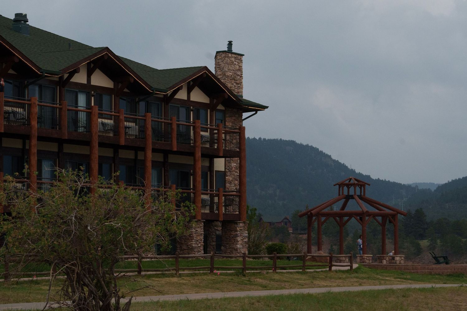 Rustic log lodge with stone accents and a wooden gazebo set against forested mountains.