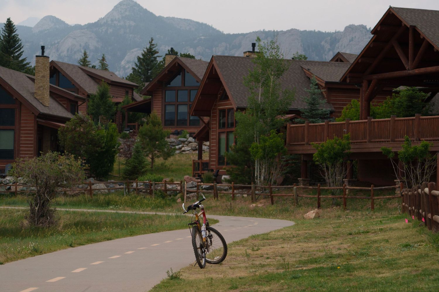 Bicycle parked on a paved path near rustic mountain lodge cabins with peaks behind.