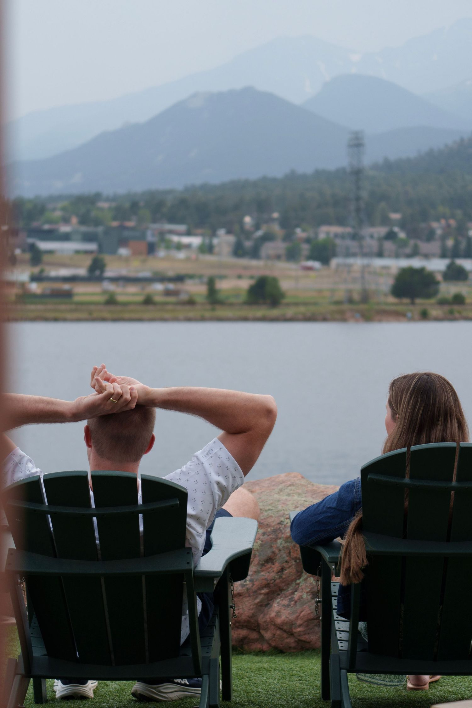 Couple relaxing in Adirondack chairs overlooking a serene mountain lake with misty peaks in the background.
