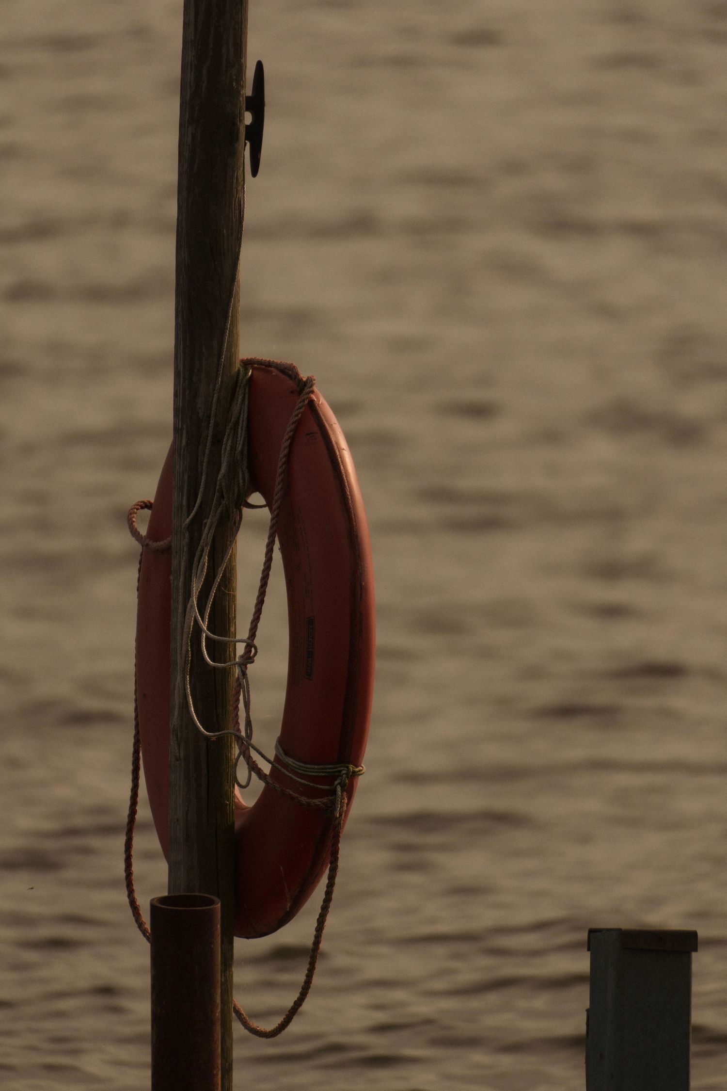 An orange life preserver ring hangs on a weathered wooden dock post above calm water.