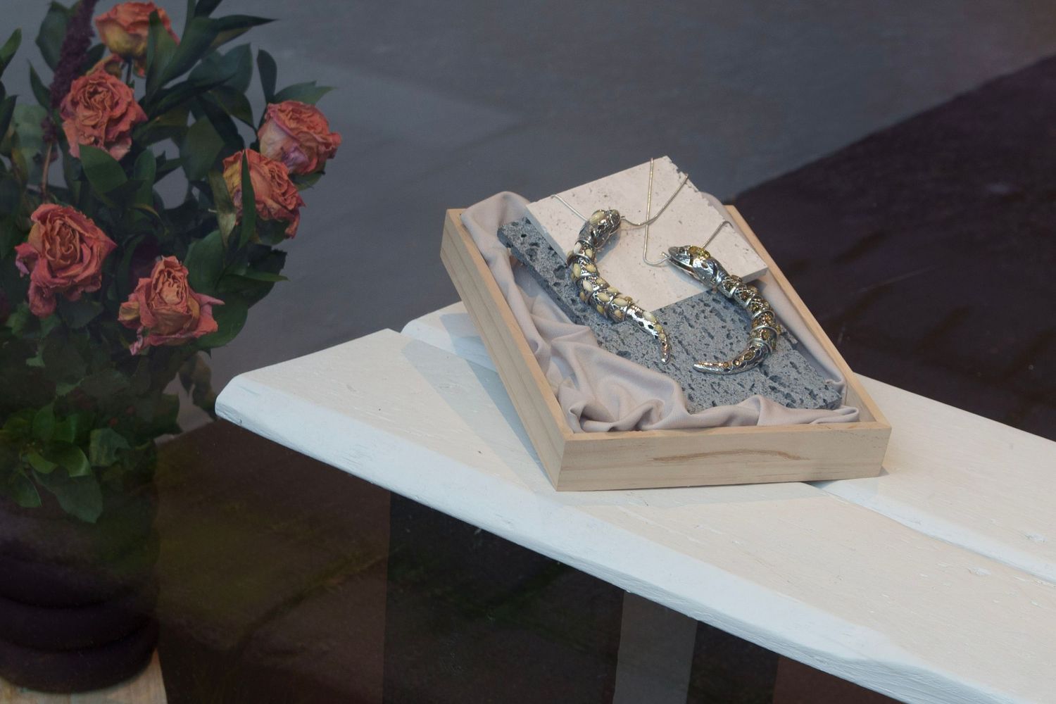 Decorative jewelry displayed in a wooden gift box on a white table beside roses.