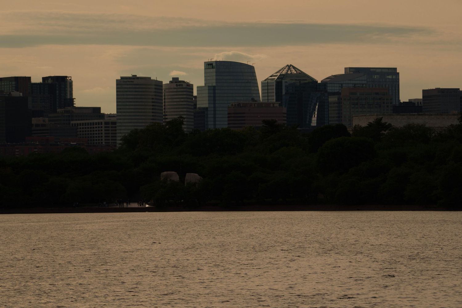 A city skyline silhouetted at dusk reflects over calm water of the Potomac River.