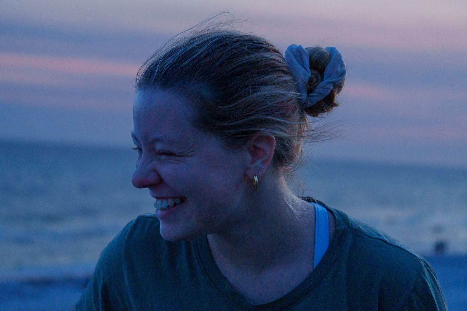 Young woman laughing at dusk by the ocean with hair in a bun.