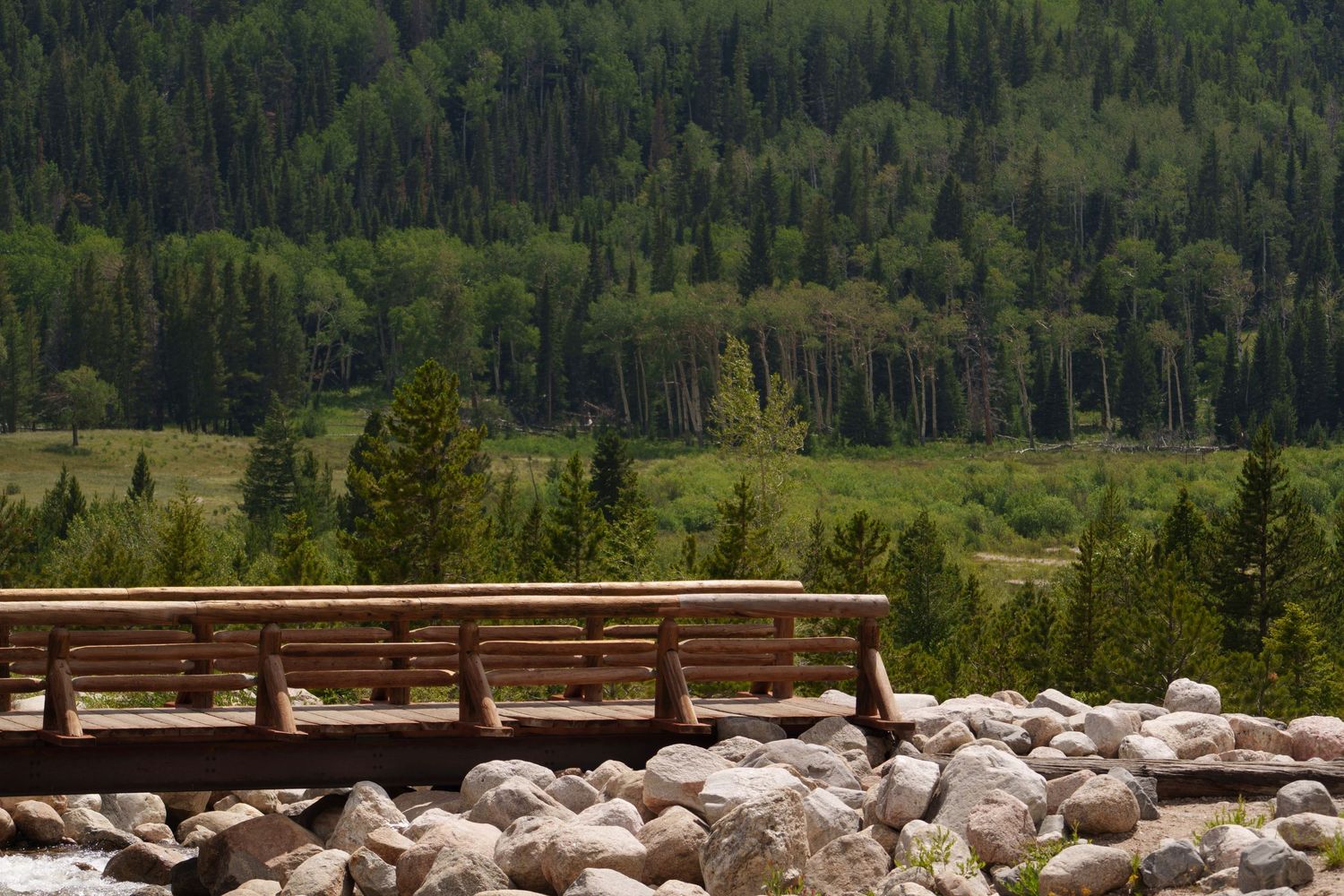 Wooden bench overlooking a rocky riverbank with a lush green forest valley beyond.