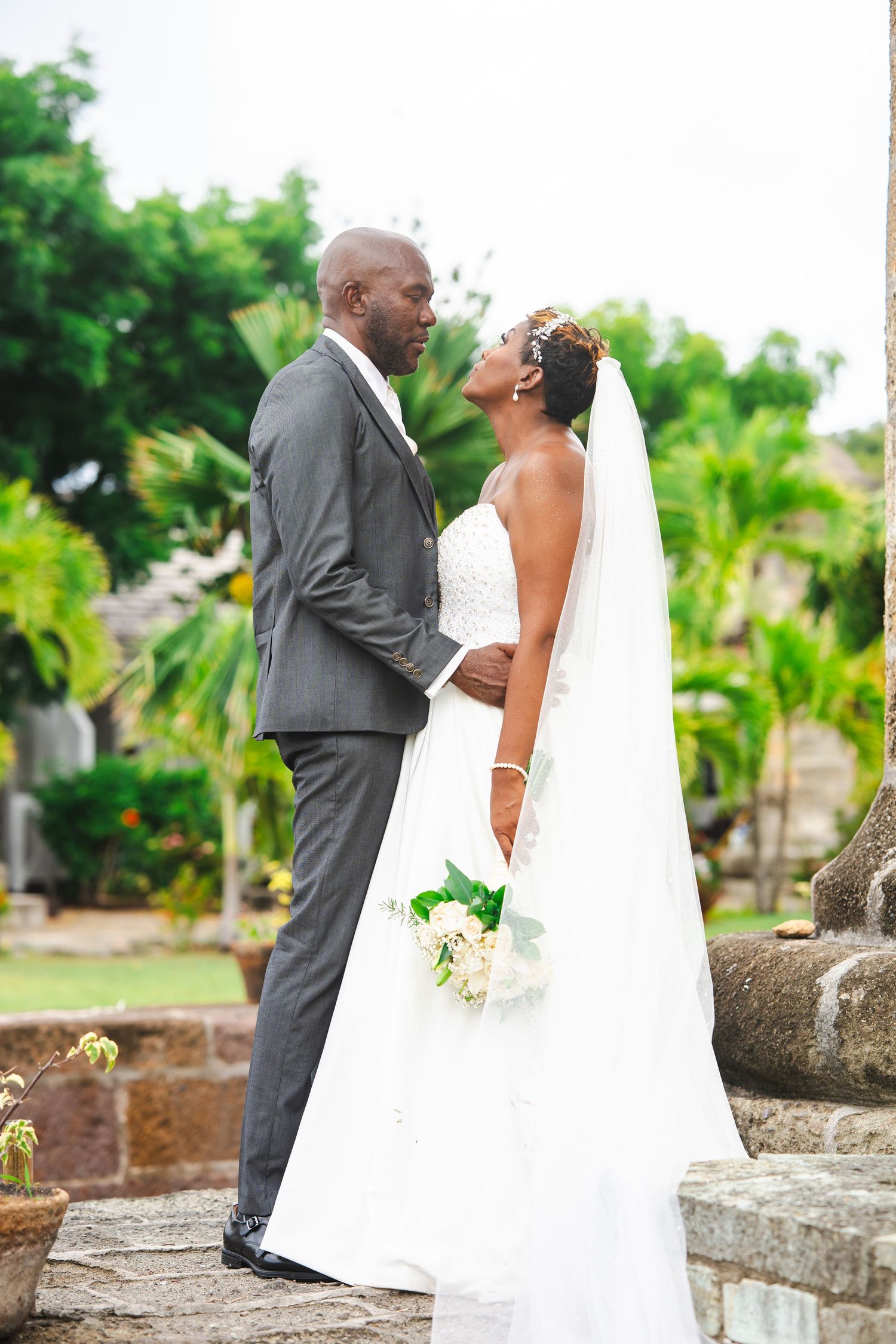 A bride and groom share a romantic moment outdoors, surrounded by lush tropical greenery on their wedding day.