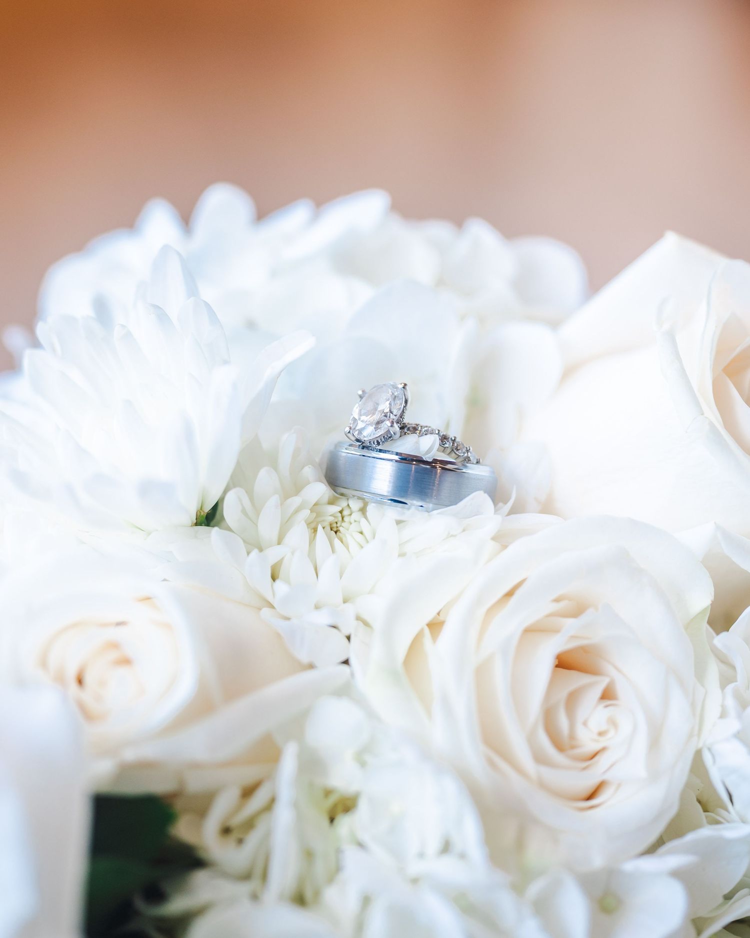 Three wedding rings nestled among white roses and chrysanthemums in a bridal bouquet close-up.