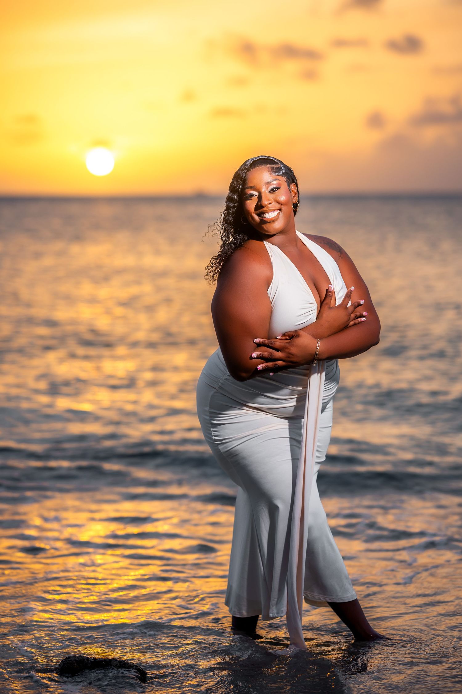 Woman in white dress posing on beach at golden sunset with ocean backdrop.