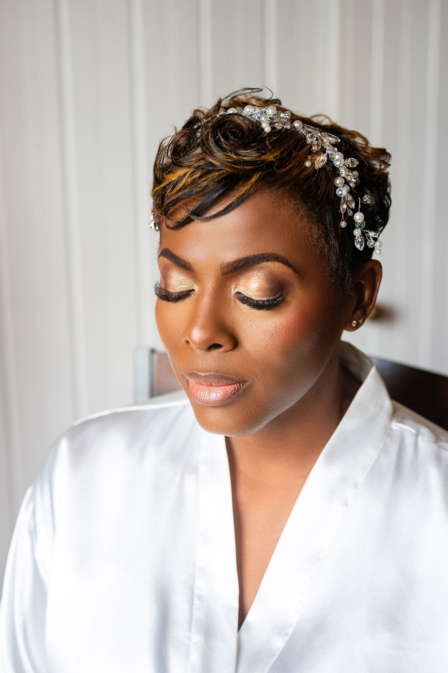 Bride with jeweled hair accessory and elegant makeup wearing a white satin robe on her wedding day.