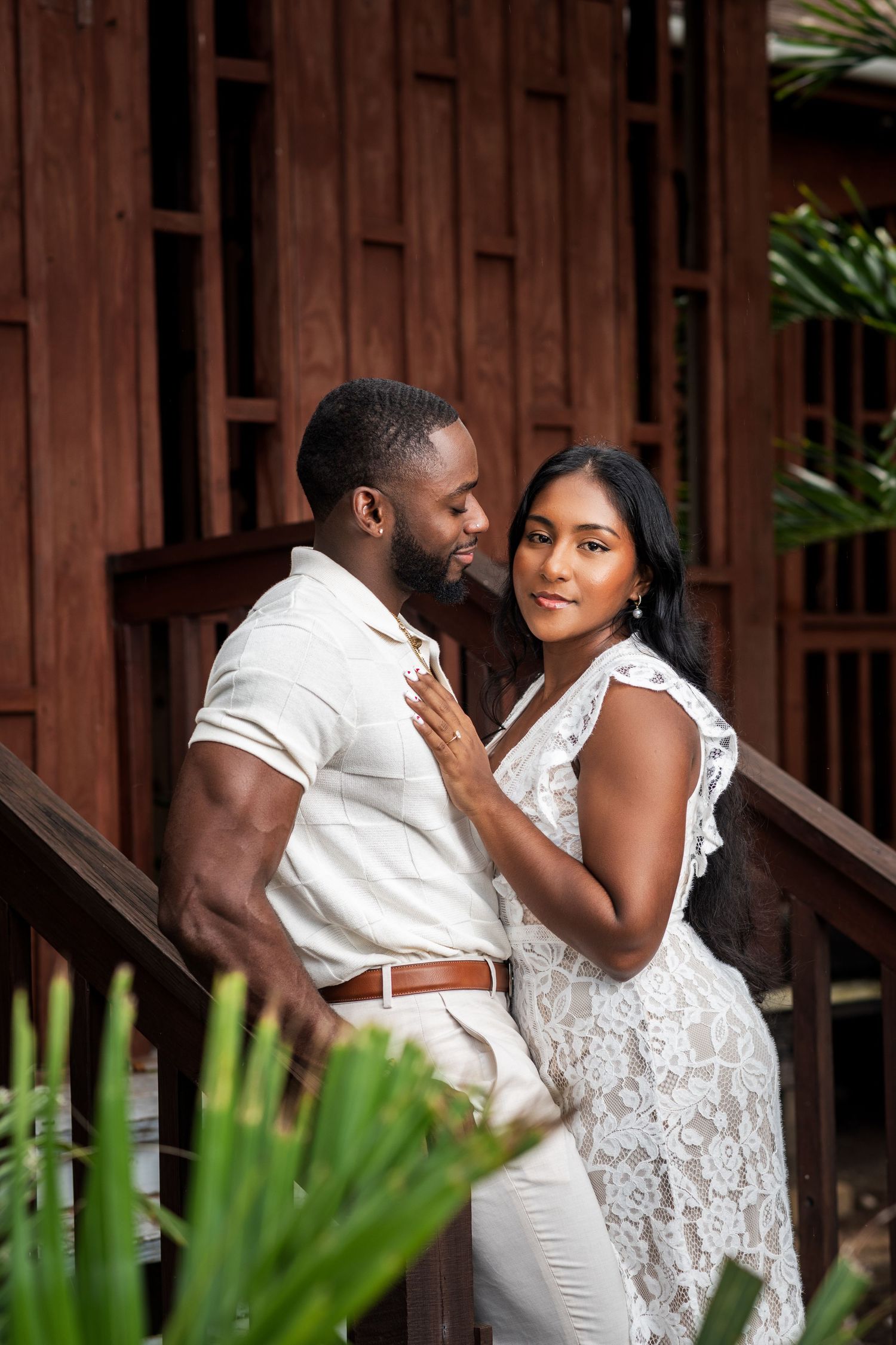 Stylish Black couple in white outfits sharing a tender moment on wooden steps.