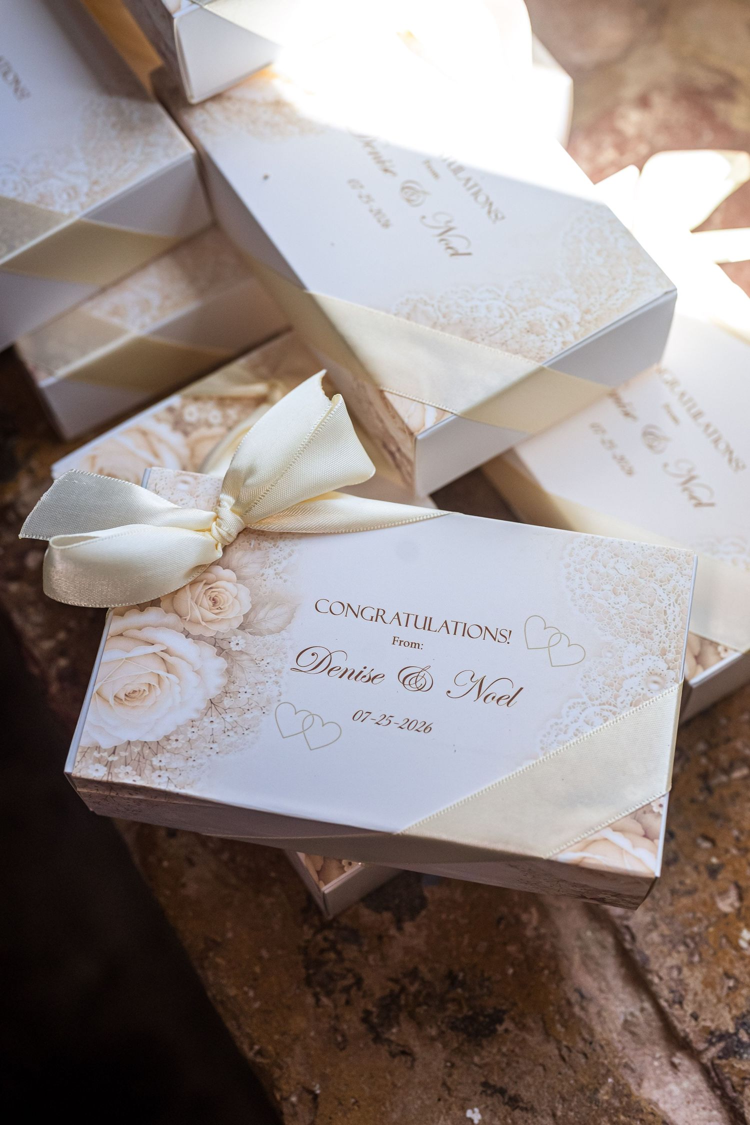 Elegant personalized wedding favor boxes with ivory ribbon bows, congratulating Denise and Noel, dated 07-23-2026.