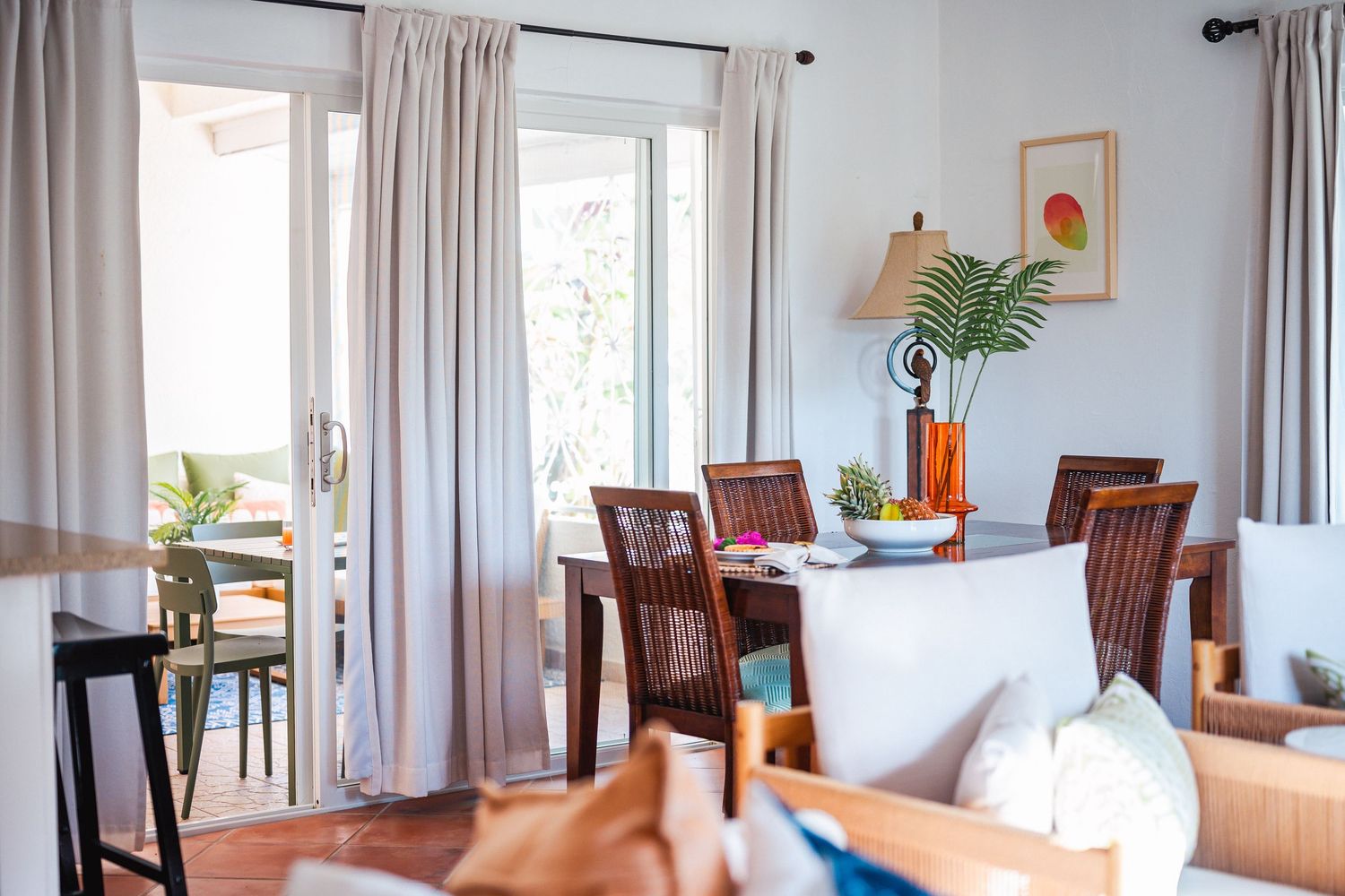 Bright dining room with wooden chairs, white curtains, and a tropical plant centerpiece near French doors.
