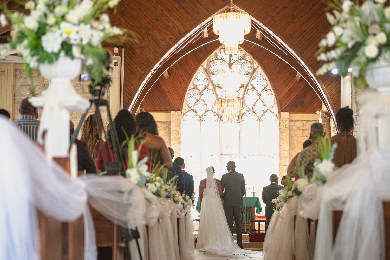 Elegant church wedding ceremony with floral arrangements lining the aisle as bride and groom stand at the altar.