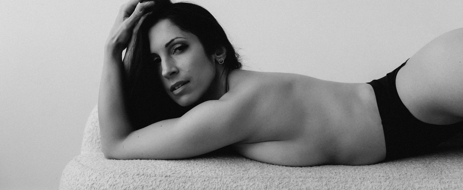 Black and white photo of a woman lying on a surface, posing elegantly in minimal clothing.