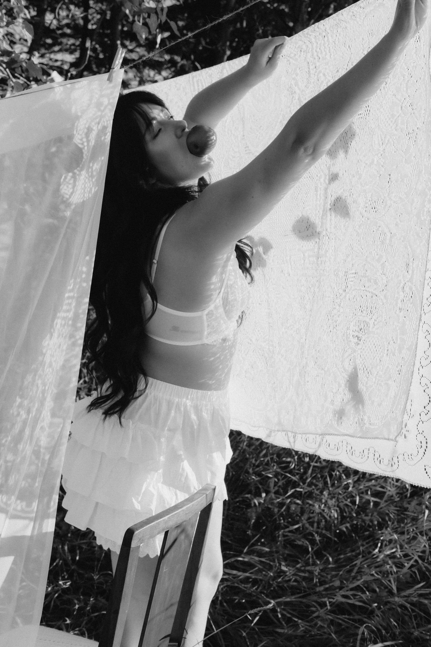 Black and white photo of a woman in white lingerie hanging laundry on a clothesline outdoors.