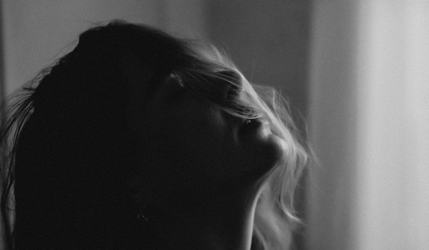 Black and white portrait of a woman with flowing blonde hair tilted back in dramatic moody lighting.
