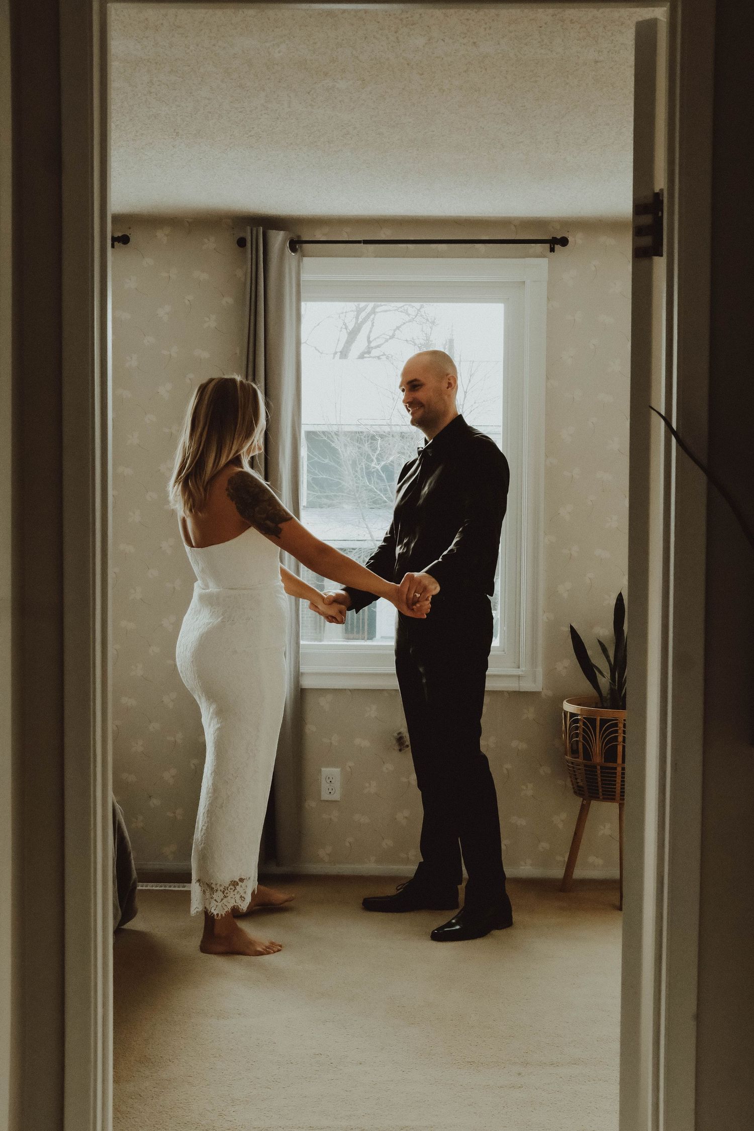 Bride and groom hold hands in doorway during romantic first look moment indoors.