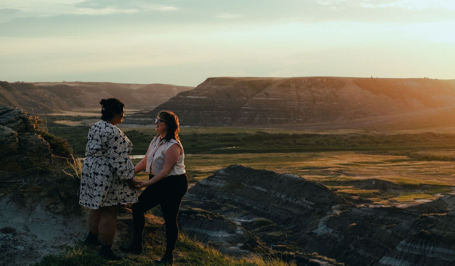 Couple sitting together on a hillside watching a golden sunset over dramatic badlands landscape.