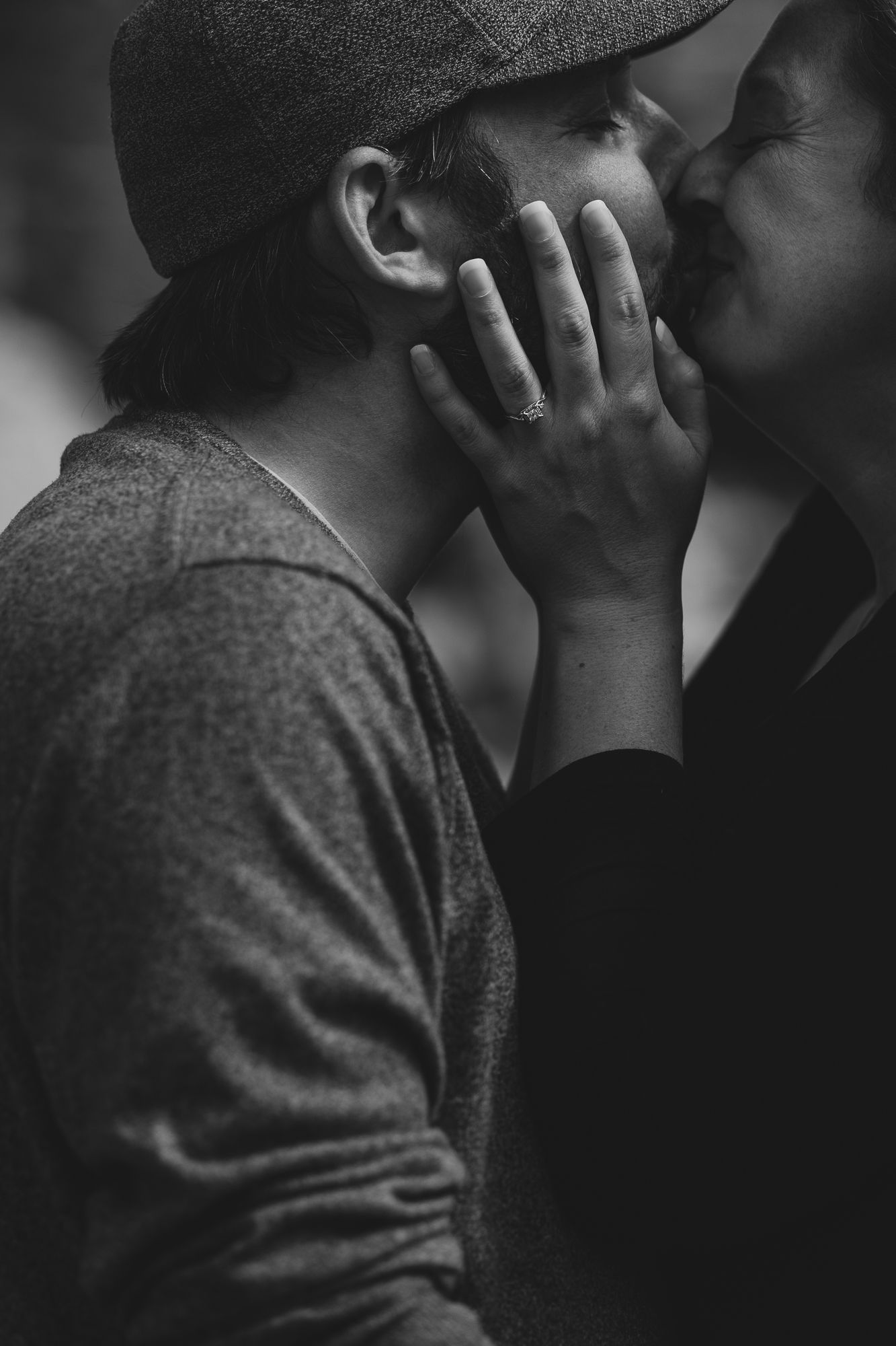 Black and white photo of a couple sharing a tender kiss, with one person wearing a flat cap.
