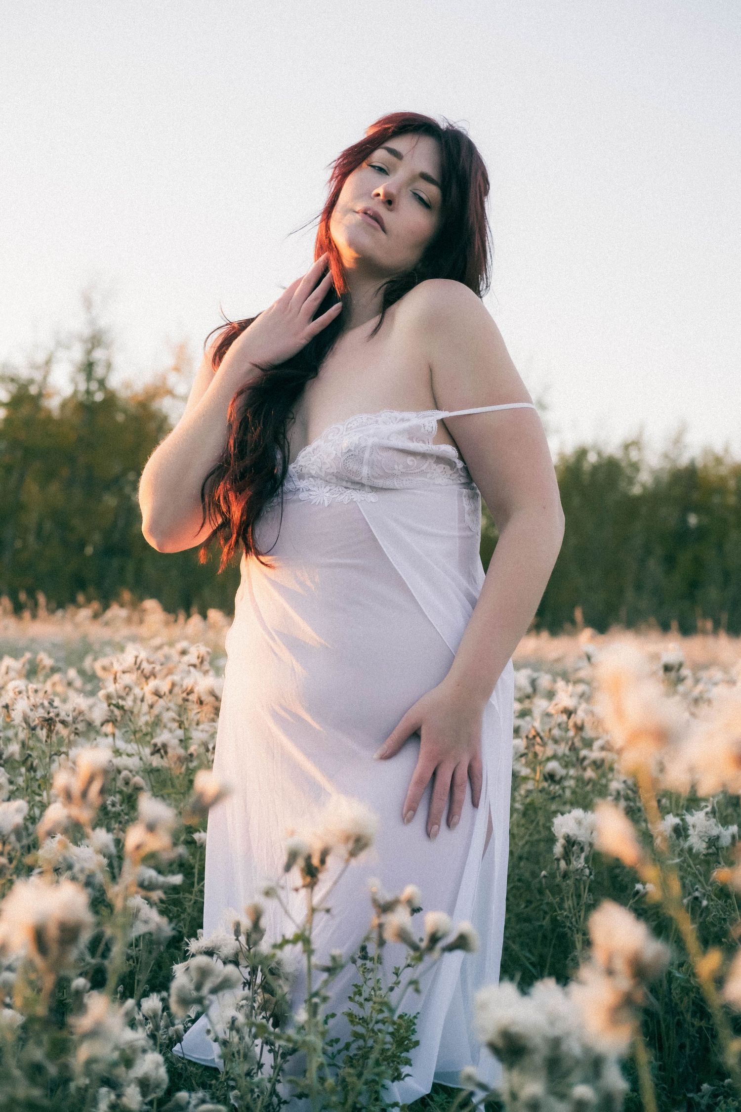 Woman in white dress standing in a field of wildflowers at golden hour sunset.