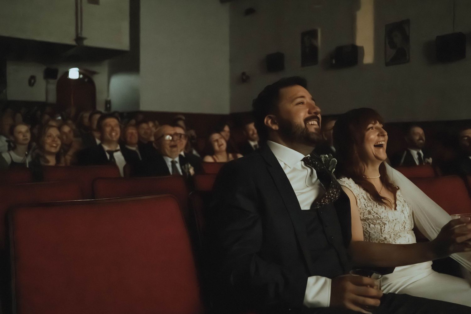 Bride and groom laughing joyfully while seated in a theater during their wedding ceremony.
