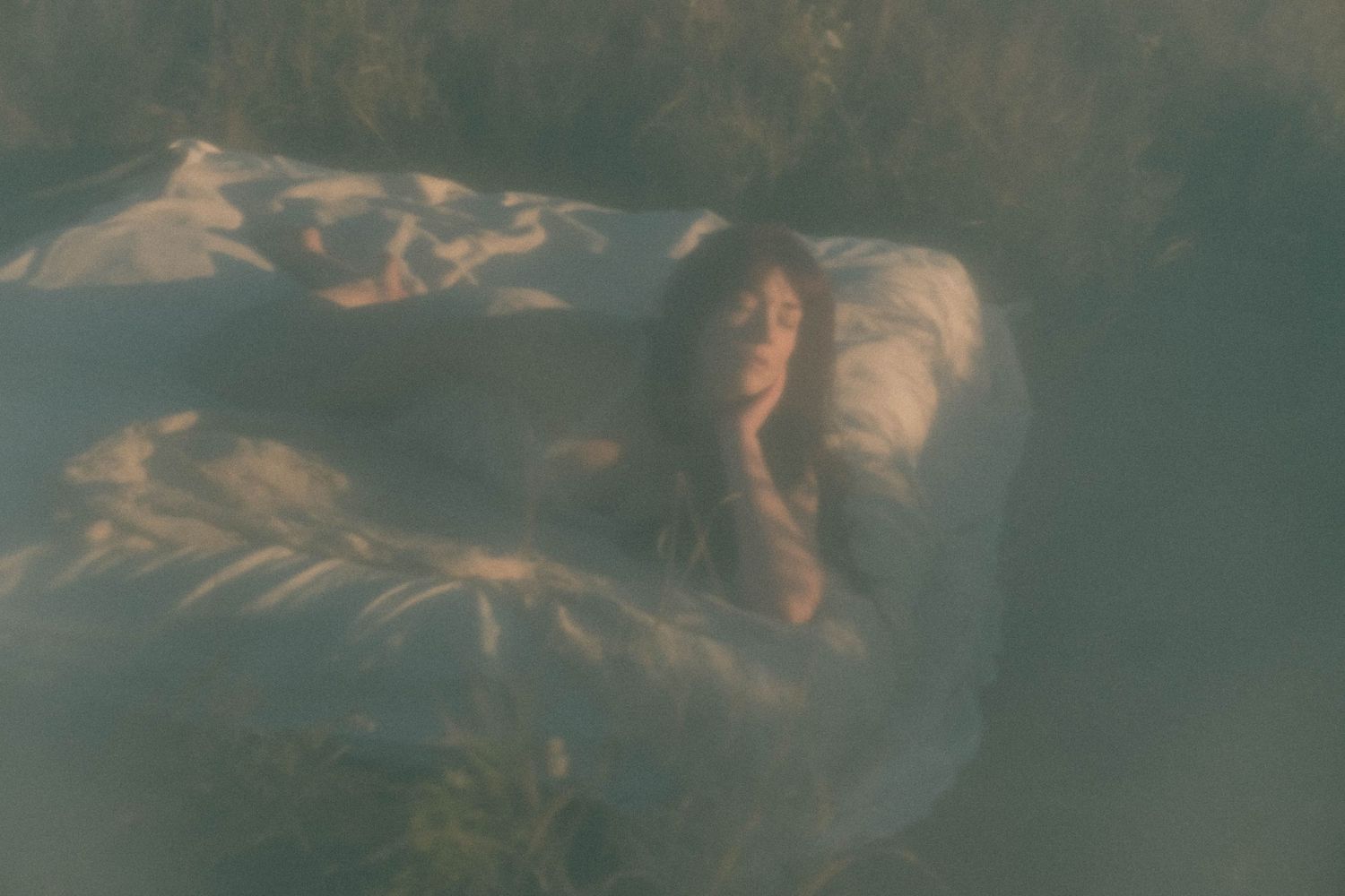 A dreamy underwater scene of a woman in flowing white fabric surrounded by aquatic plants in soft green hues.