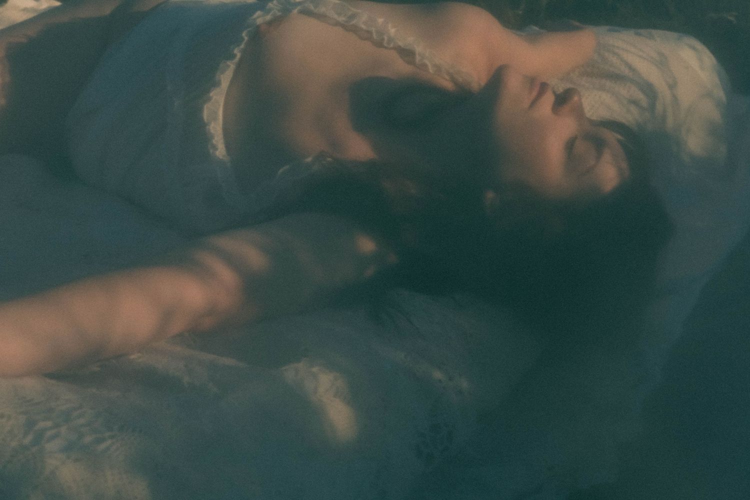 A woman with white hair floats serenely in dark water wearing a lace top, ethereal and dreamlike.