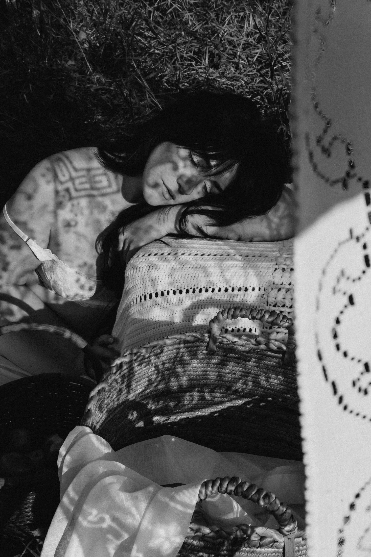 Black and white photo of woman resting on blanket in sunlit grass.